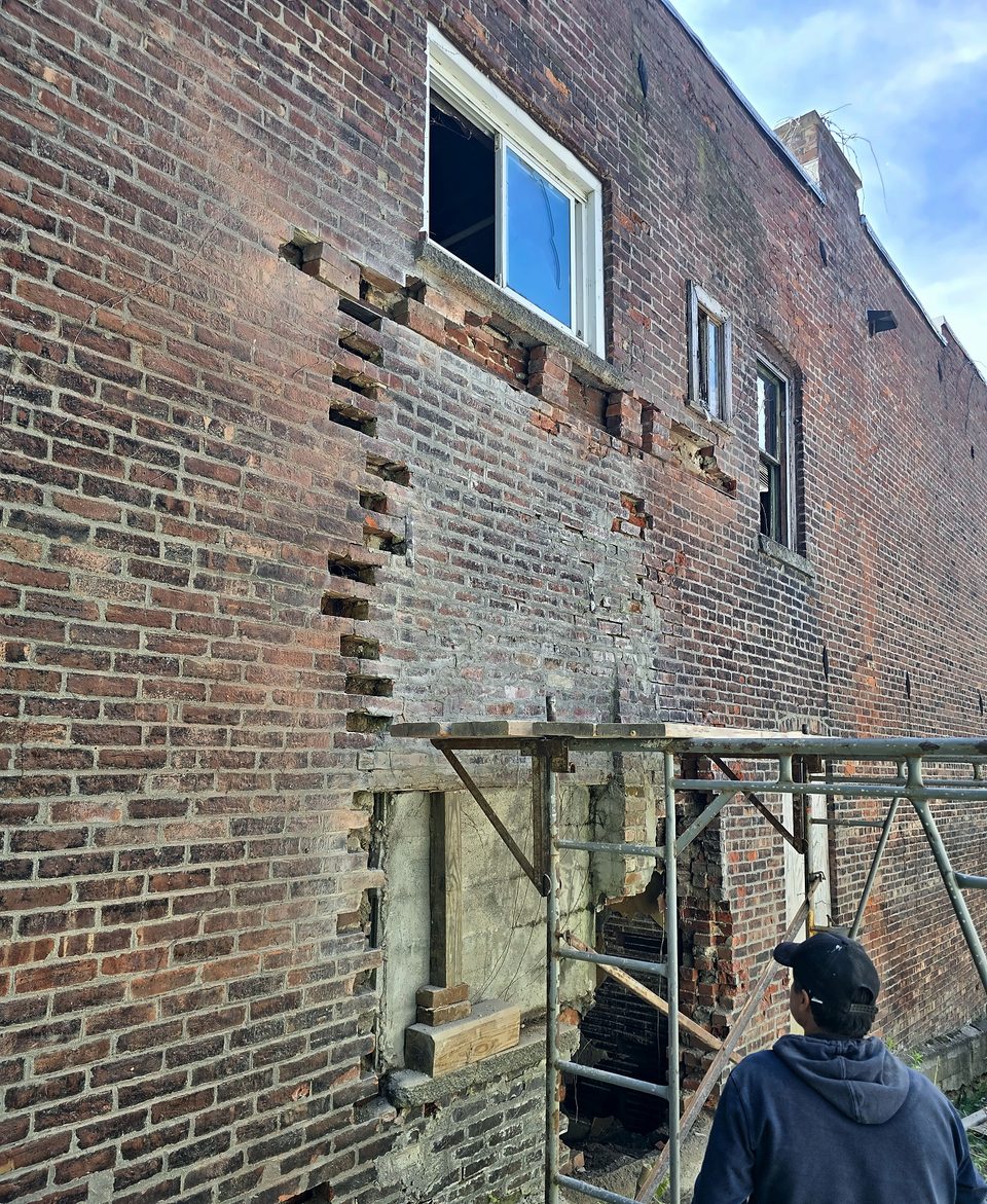Mason on pipe scaffold toothing new brick into a rebuilt wall in Troy